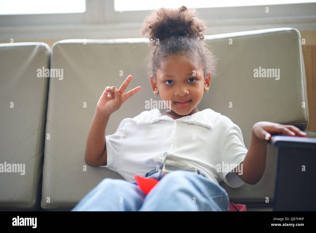 Porträt eines afroamerikanischen Kindes, das auf dem Sofa mit beweglicher Divice sitzt. Stockfoto