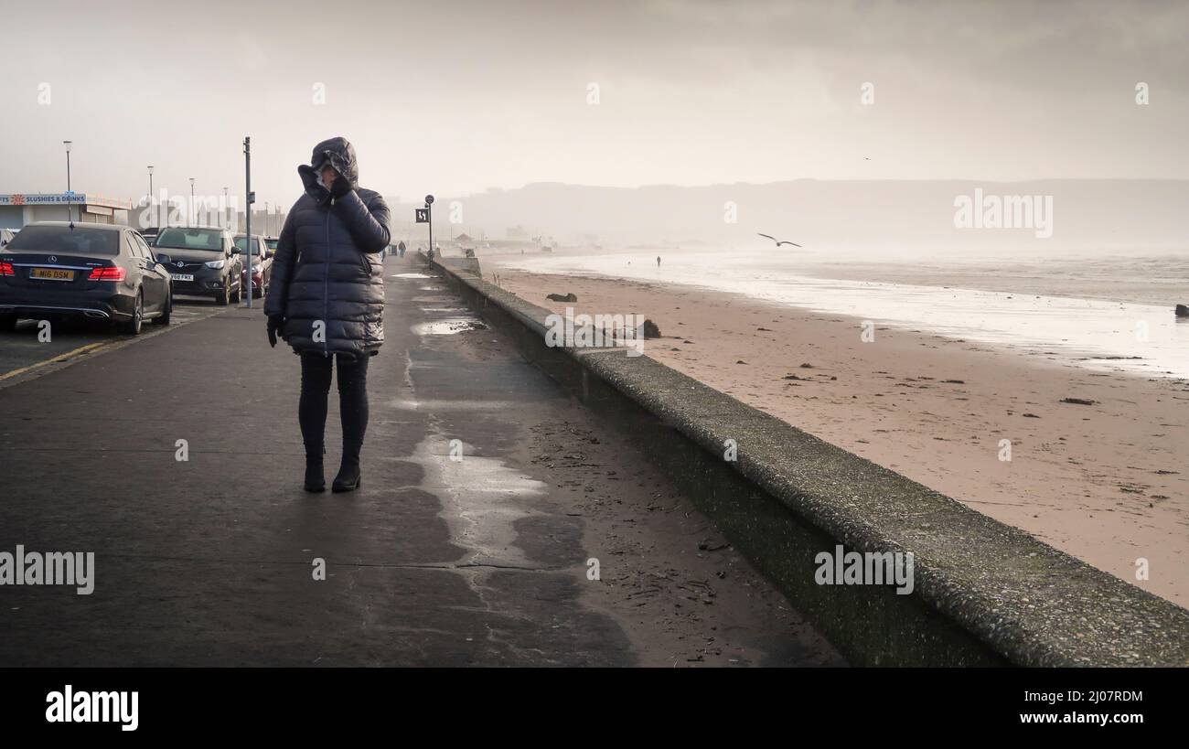 Frau, die im Saitenwind an der Küste von Ayr läuft Stockfoto