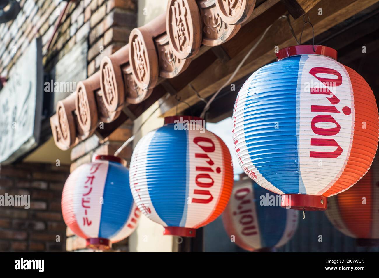 Nahaufnahme von roten, blauen und weißen hängenden Papierlaternen aus Japan, die Orion-Bier vor einem Okinawa-Restaurant in Nara, Japan, fördern Stockfoto