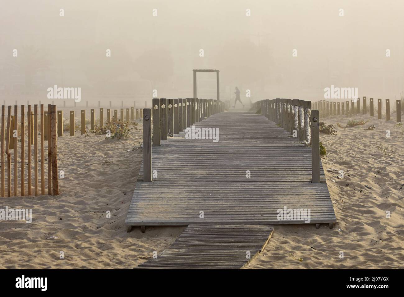 Holzsteg, Mann, der im Morgennebel am Strand läuft, Figueira da Foz Portugal. Stockfoto