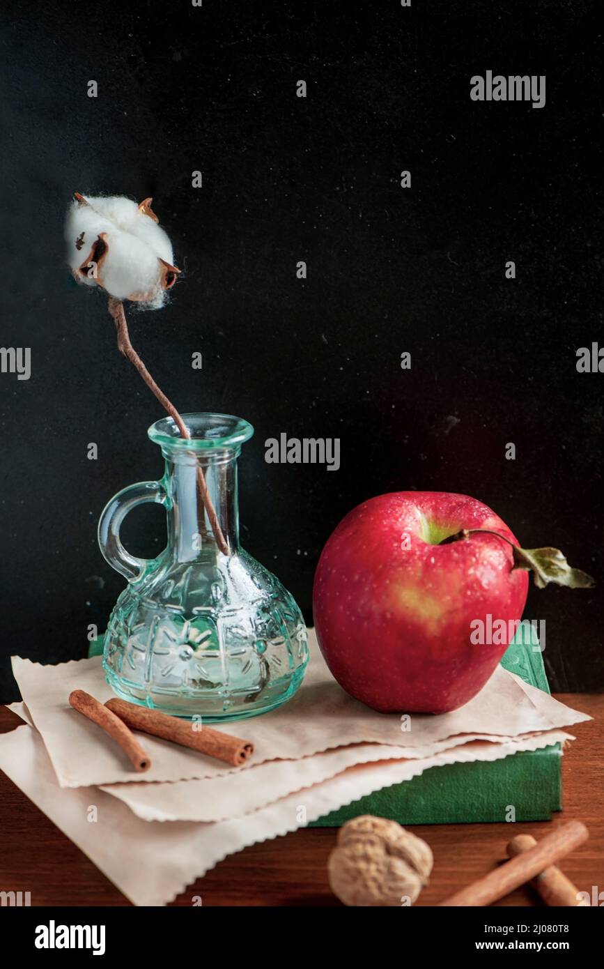 Baumwollknospe, roter Apfel und altes Buch und Papier auf einem Holztisch, Nahaufnahme, Stillleben Fotografie Stockfoto