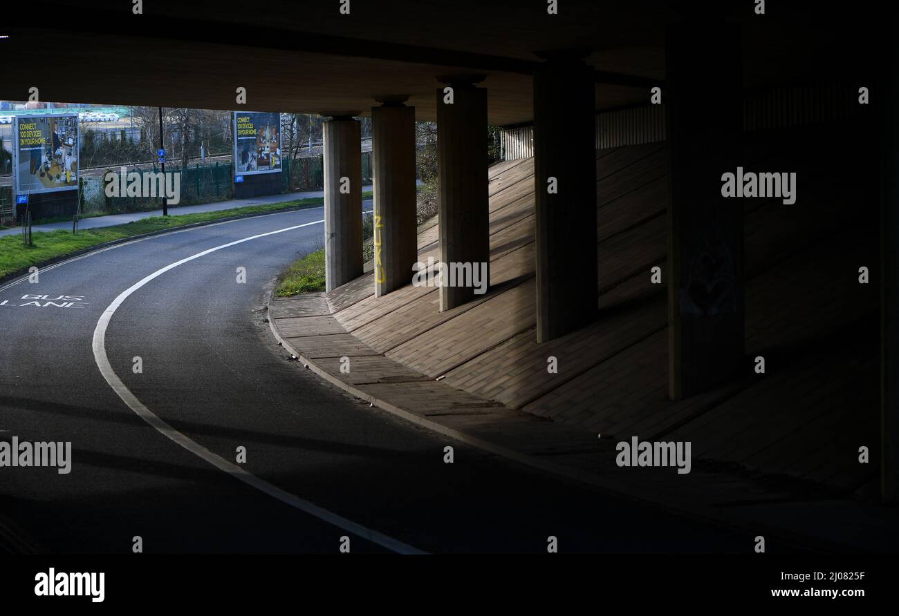 Eine leere Unterführung mit Straßenüberführung, die Stützsäulen und Straßen in Schatten und Licht zeigt. Stockfoto