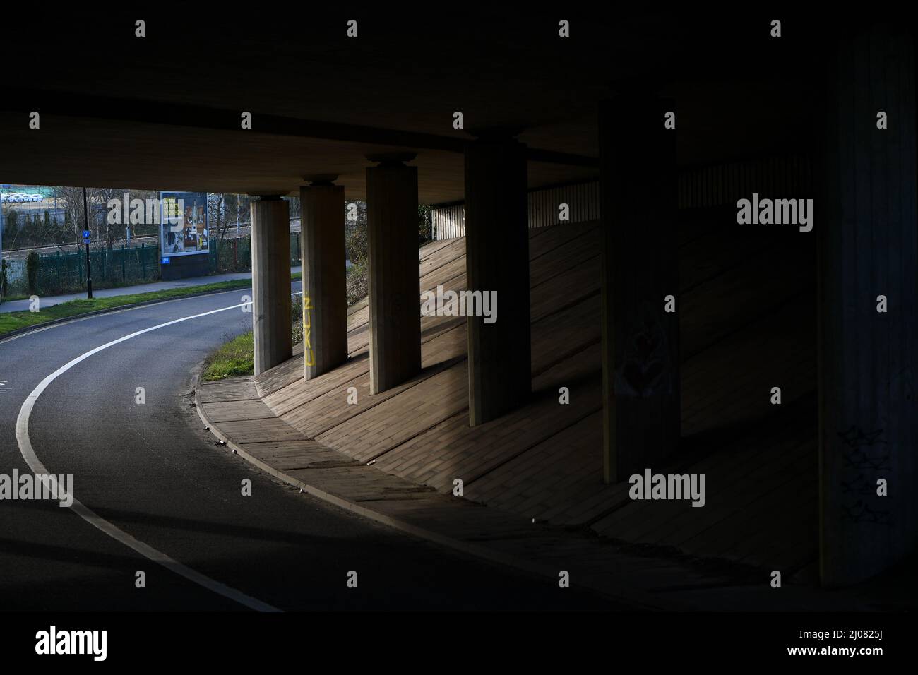 Eine leere Unterführung mit Straßenüberführung, die Stützsäulen und Straßen in Schatten und Licht zeigt. Stockfoto