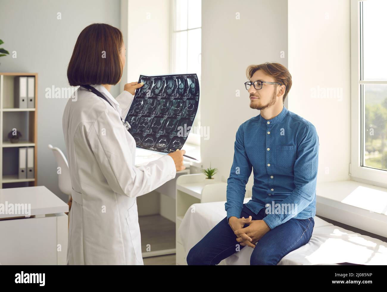 Medizinische Fachärztin, die sich ein Röntgenbild ansieht, während sie mit ihrer jungen Patientin spricht Stockfoto