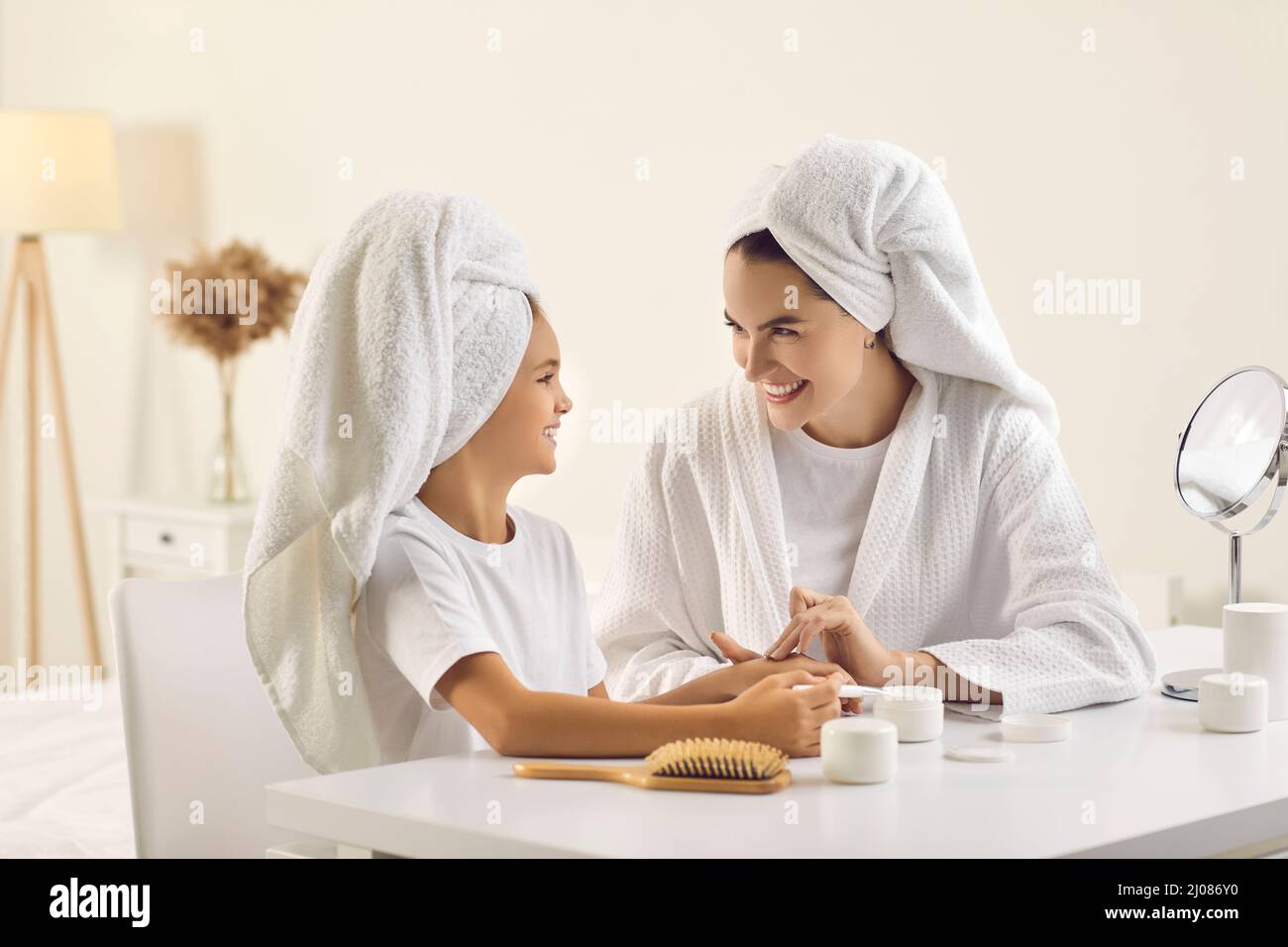 Glückliche, schöne Mutter und Tochter in weißen Handtüchern, die gemeinsam die Hautpflegeroutine machen Stockfoto