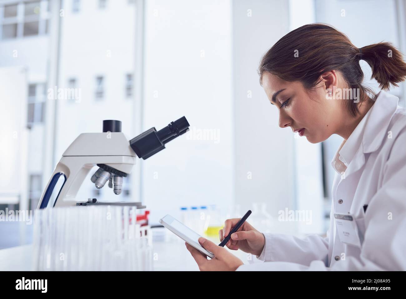 Forschung ist nur ein Teil der Arbeit. Aufnahme einer fokussierten jungen Wissenschaftlerin, die an einem digitalen Tablet arbeitet, während sie in einem Labor sitzt. Stockfoto