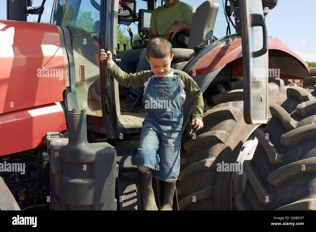 Das war ein harter Arbeitstag. Aufnahme eines kleinen Jungen, der von einem Traktor herunterklettert. Stockfoto