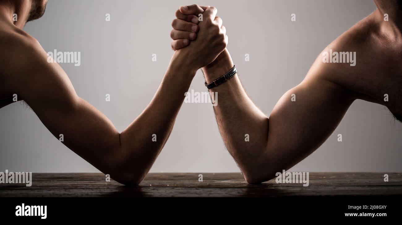 Stark muskulös bärtiger Mann, der einen schwach schwachen Mann am Arm kämpft. Arme ringen dünne Hand, großer starker Arm im Studio. Zwei Männerhände umklammten Arm-Wrestling Stockfoto