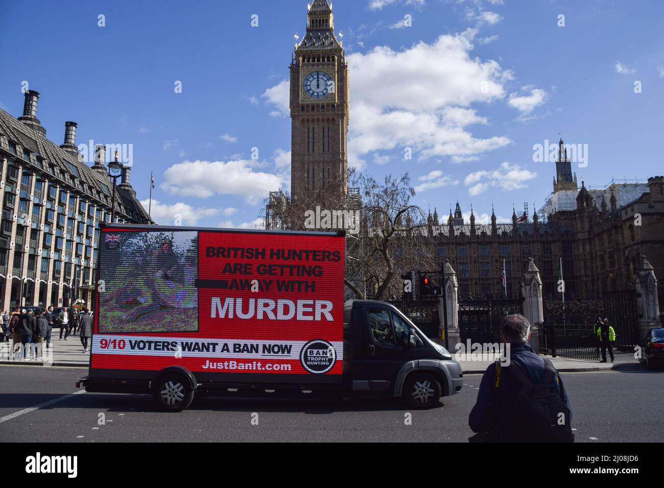 London, Großbritannien. 17. März 2022. Ein Werbewagen fährt mit einem digitalen Bildschirm an den Houses of Parliament vorbei, auf dem ein Bild eines Jägers mit einem toten Löwen und die Worte „Britische Jäger kommen mit Mord weg“ zu sehen sind. Die Organisation Campaign to Ban Trophy Hunting führt die Kampagne derzeit als Reaktion auf die potenziellen Pläne der britischen Regierung aus, ein geplanes Verbot von Importen für die Trophäenjagd zu streichen. Kredit: ZUMA Press, Inc./Alamy Live Nachrichten Stockfoto