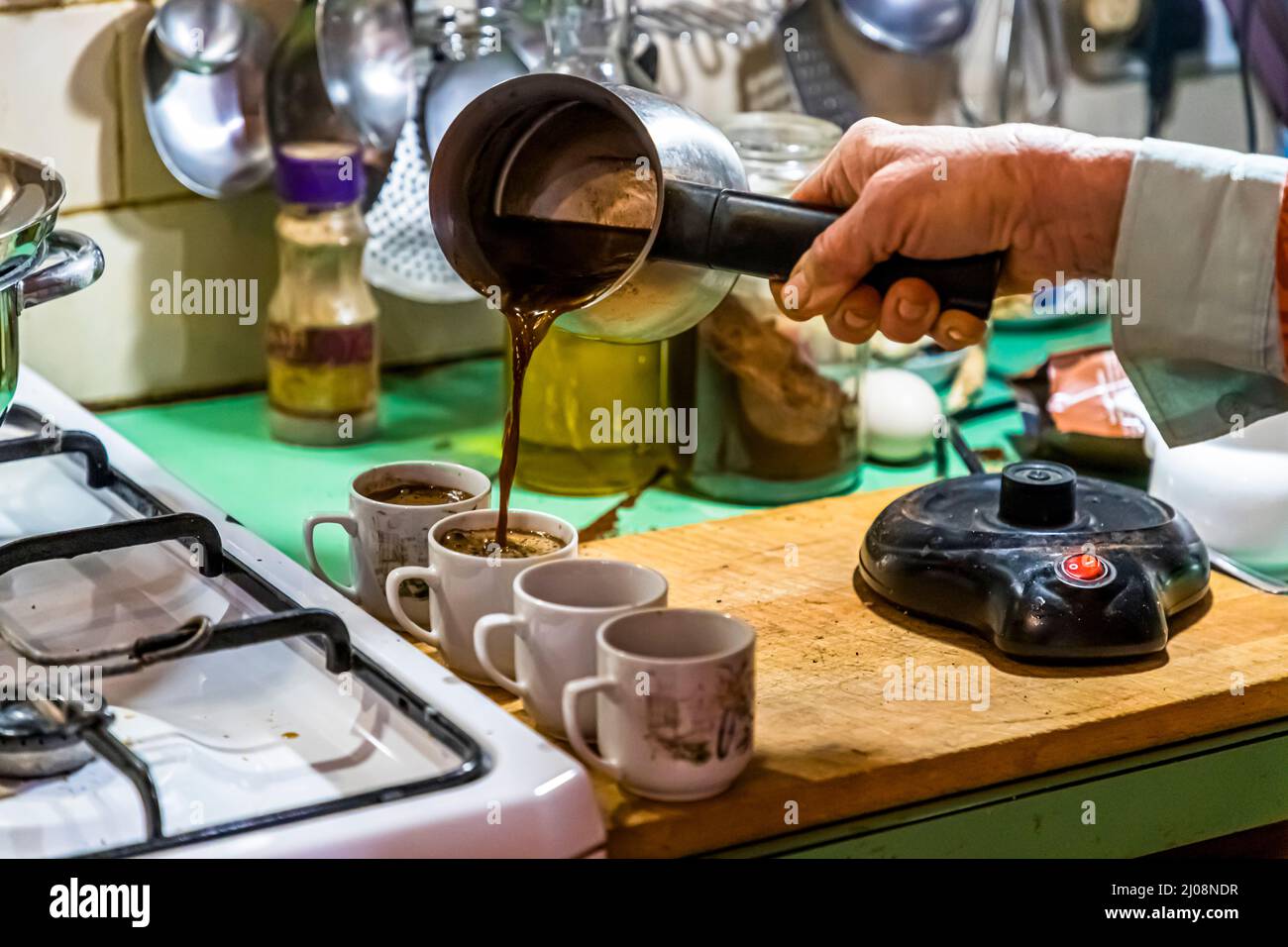 Eine Hand gießt Türkischen Kaffee aus einem Cezve-Topf in kleine Tassen auf einer Küchentheke auf der Delcraft-Farm in Büyükkonuk (Komi Kebir), Türkische Republik Zypern (TRNK). Stockfoto