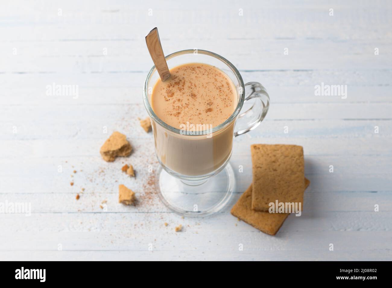 Würziger, wärmender Tee mit Milch in einer Glastasse und Lebkuchenkeks auf hellgraublauem Hintergrund Stockfoto