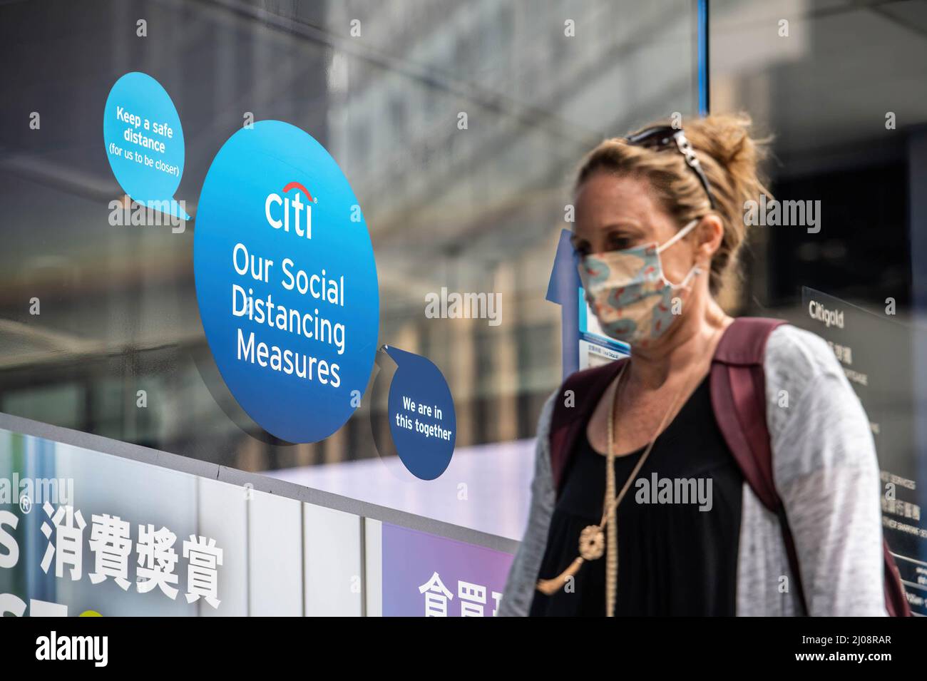 Eine Frau, die eine OP-Maske trägt, kommt an einem Outlet der Citi Bank im Central Business District von Hongkong vorbei. Nach der wirtschaftlichen Analyse der Regierung von Hongkong steht der Einzelhandel kurzfristig unter immensem Druck, da die Pandemie und die damit verbundenen sozialen Distanzierungsmaßnahmen eine Herausforderung für eine Wiederbelebung darstellen. Stockfoto