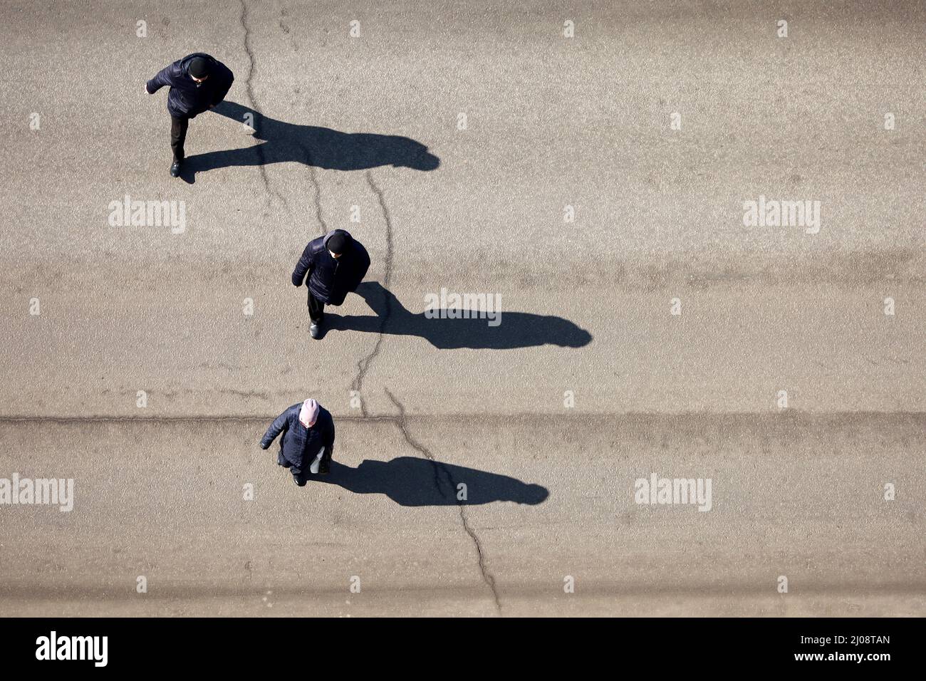 Menschen, die die Straße überqueren, Draufsicht. Lange Schatten auf Asphalt, Konzept der Verkehrssicherheit, Stadtleben Stockfoto