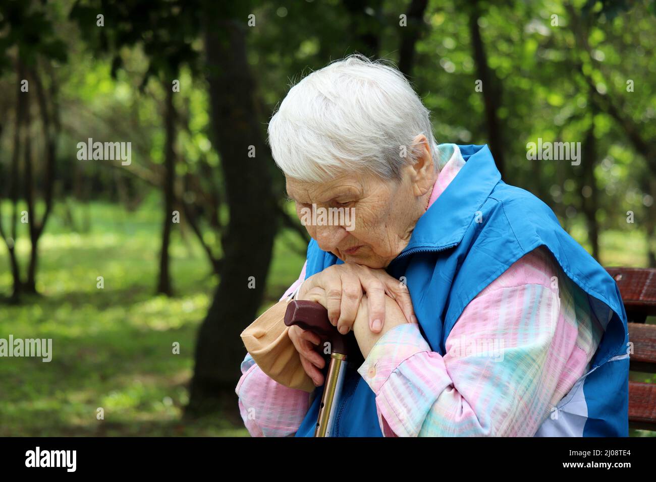 Porträt einer älteren grauhaarigen Frau, die mit Gehstöcken auf einer Bank in einem Park sitzt. Gesunde Lebensweise im Alter, Leben im Ruhestand Stockfoto