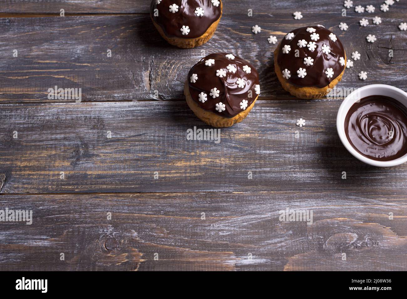 Würzige Kürbis-Muffins mit Nüssen, verziert mit Schokoladenglasur und Zucker Schneeflocken unter dem Weihnachtsbaum auf einem Holztisch, Freiraum, selektiv Stockfoto