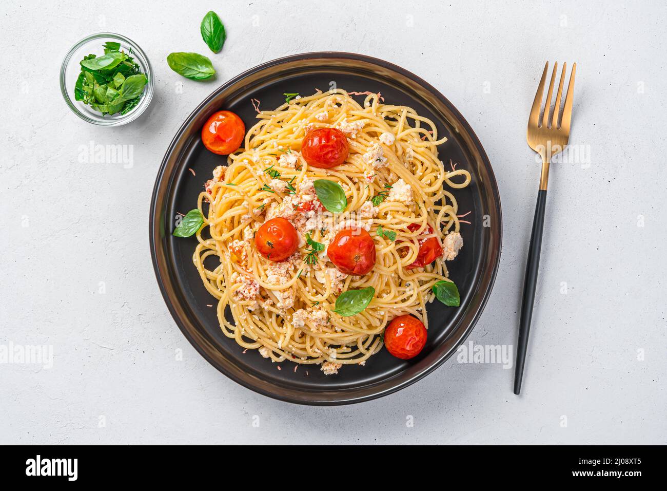 Fetapasta in einer schwarzen Platte auf grauem Hintergrund. Gebackene Feta mit Kirschtomaten. Draufsicht. Stockfoto