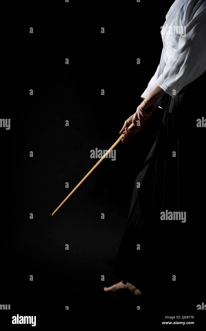 Ein Mädchen in schwarzem Hakama, das in kämpfender Pose mit Holzschwert auf dunklem Hintergrund bokken steht. Geringe Schärfentiefe. SDF. Stockfoto