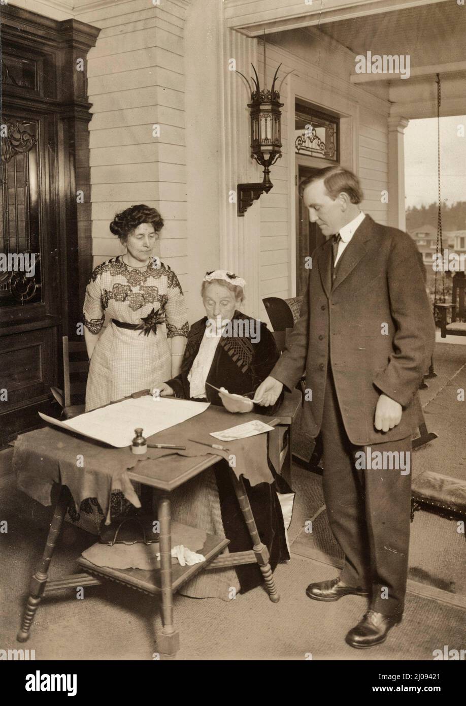 Abigail Scott Duniway unterschrieb die erste Proklamation für gleiches Wahlrecht, die jemals von einer Frau verkündet wurde. Der Gouverneur von Oregon, Oswald West, der die Proklamation unterzeichnet hatte, wird mit Blick auf die Proklamation gezeigt, und die amtierende Präsidentin Dr. Viola M. Coe steht in der Nähe - November 1912 Stockfoto