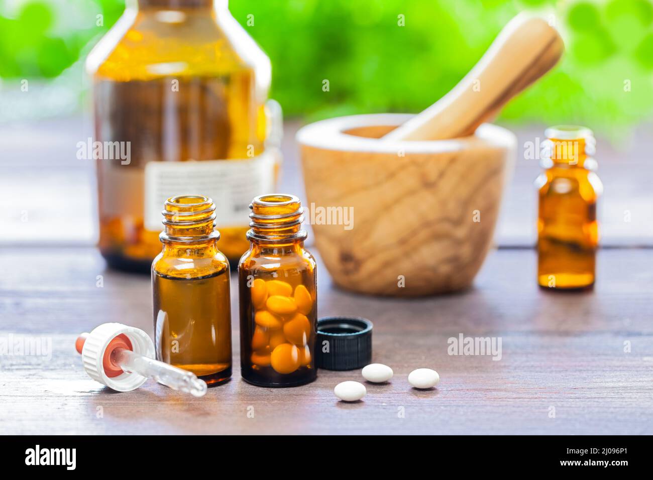 Ein Holzmörtel und Stößel mit einigen braunen medizinischen Flaschen und Pillen auf einem Holztisch. Homöopathisches Konzept. Fokus auf den Vordergrund. Stockfoto