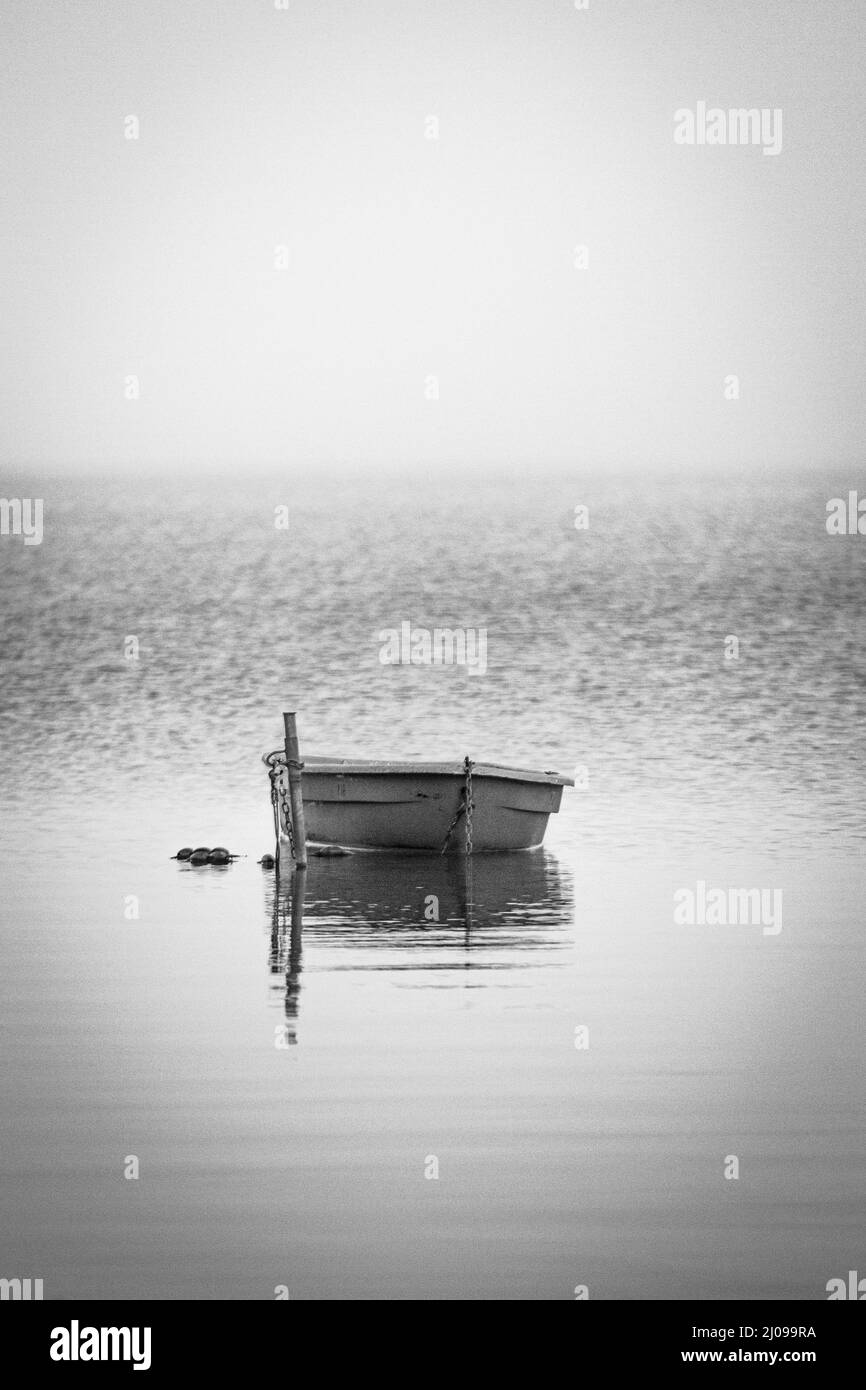 Vertikale schwarz-weiße Aufnahme eines Wasserkörpers mit einem kleinen Boot ohne Menschen Stockfoto