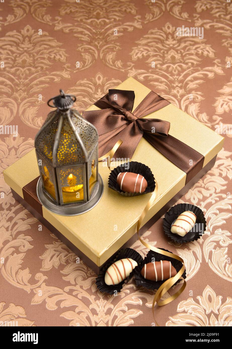 Traditionelle Ramadan-Lampe auf goldener Geschenkbox zusammen mit Dattel-Schokolade. Islamischer festlicher Hintergrund. Stockfoto