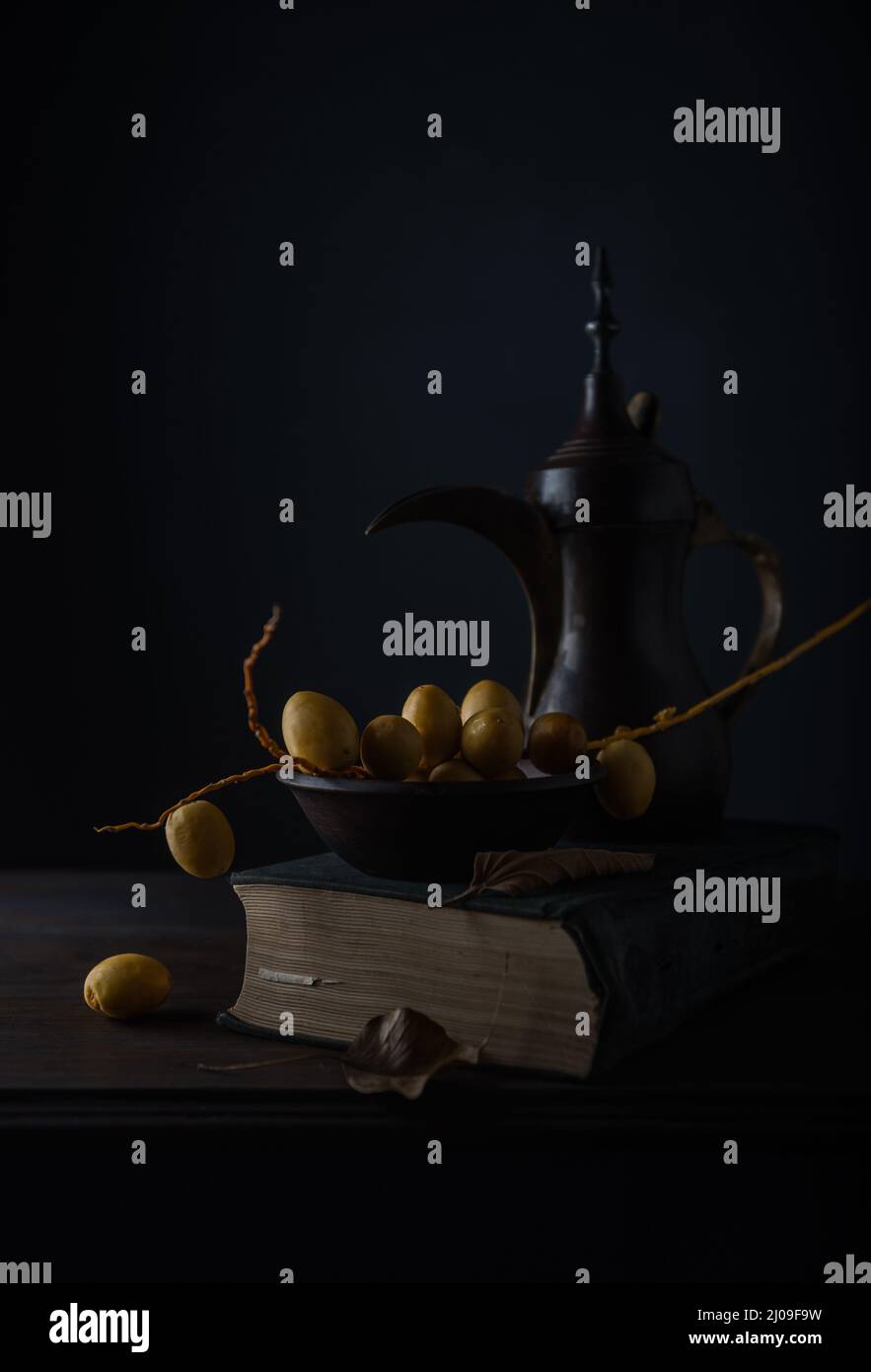 Schönes, rustikales Stillleben Foto mit einer antiken arabischen Kaffeekanne oder Dallah und Datteln. Unreife Datteln und alte Arabische Kaffeekanne aus Metall. Stockfoto