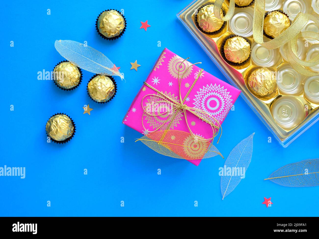 Schönes Foto von Schokolade und eine Geschenkbox mit Konfetti um. Draufsicht auf eine Schachtel mit Schokoladentablett und eine verpackte Geschenkbox. Stockfoto