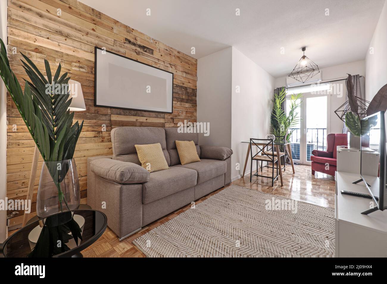Wohnzimmer mit Wandbelägen, Palmenblatt in einer Glasvase, grauem Zweisitzer-Sofa und Naturfaserteppich Stockfoto