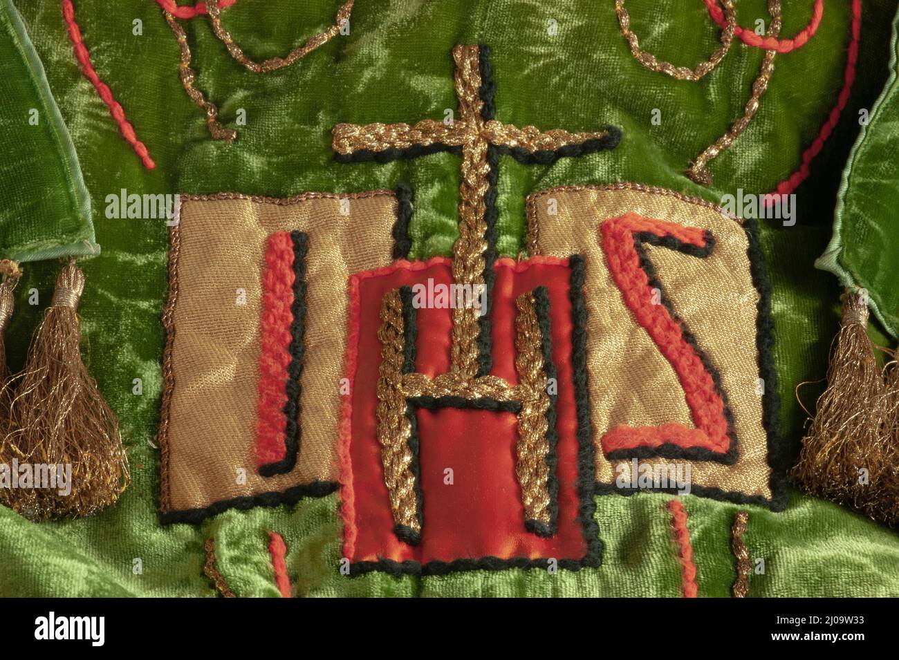 Dies ist eine Nahaufnahme eines in Frankreich hergestellten christlichen Gewandes, der das Wort Jesus mit einem zentralen gestickten goldenen Kreuz darstellt. Grün bedeutet Wachstum. Stockfoto
