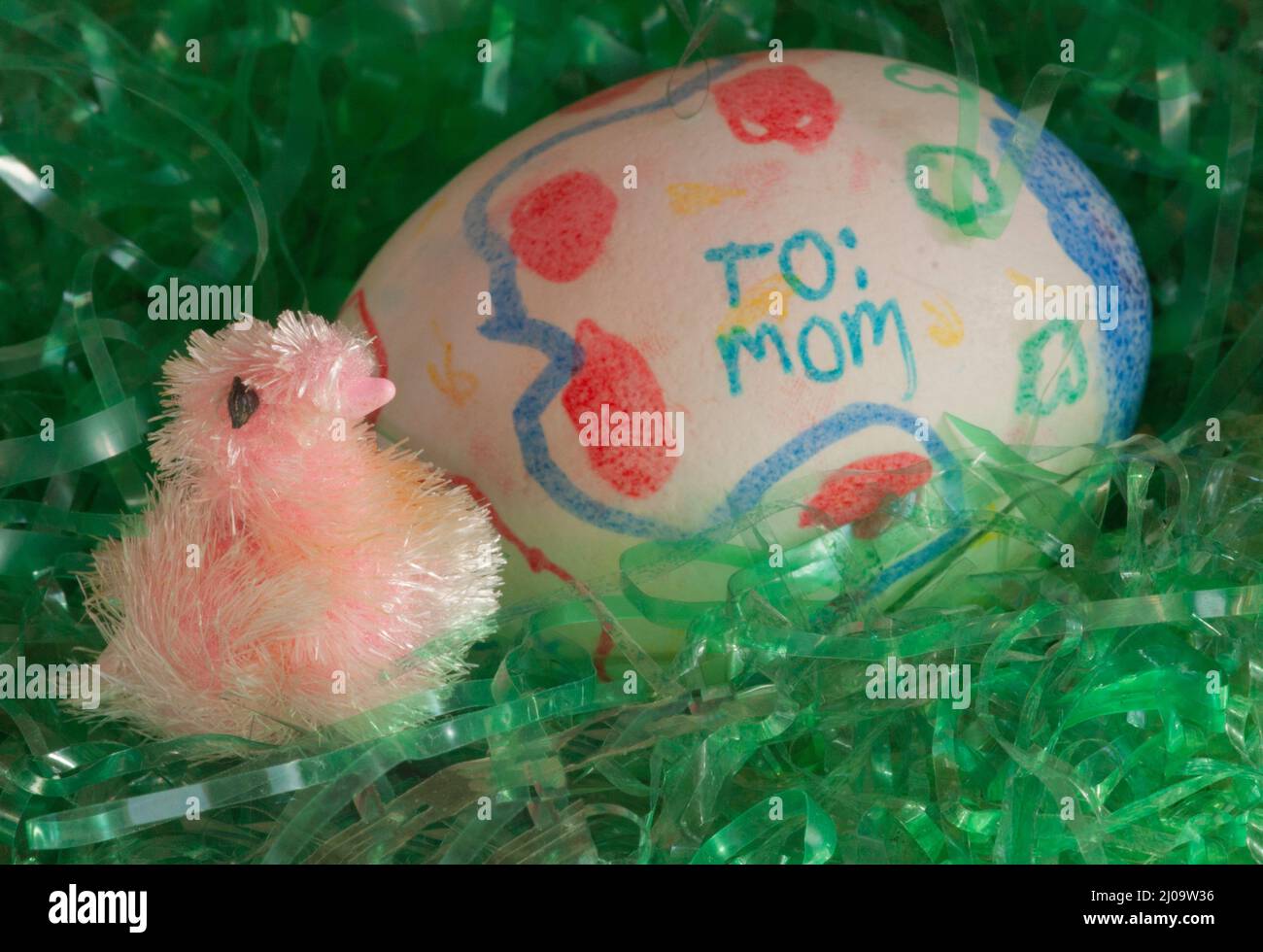 „To Mom“-Hand, die von einem Kind auf einem DIY-Kind geschrieben wurde, das Osterei dekoriert hat. Das Ei wird mit einem fuzzy Baby Küken auf grünem Ostergras platziert.Nahaufnahme. Stockfoto
