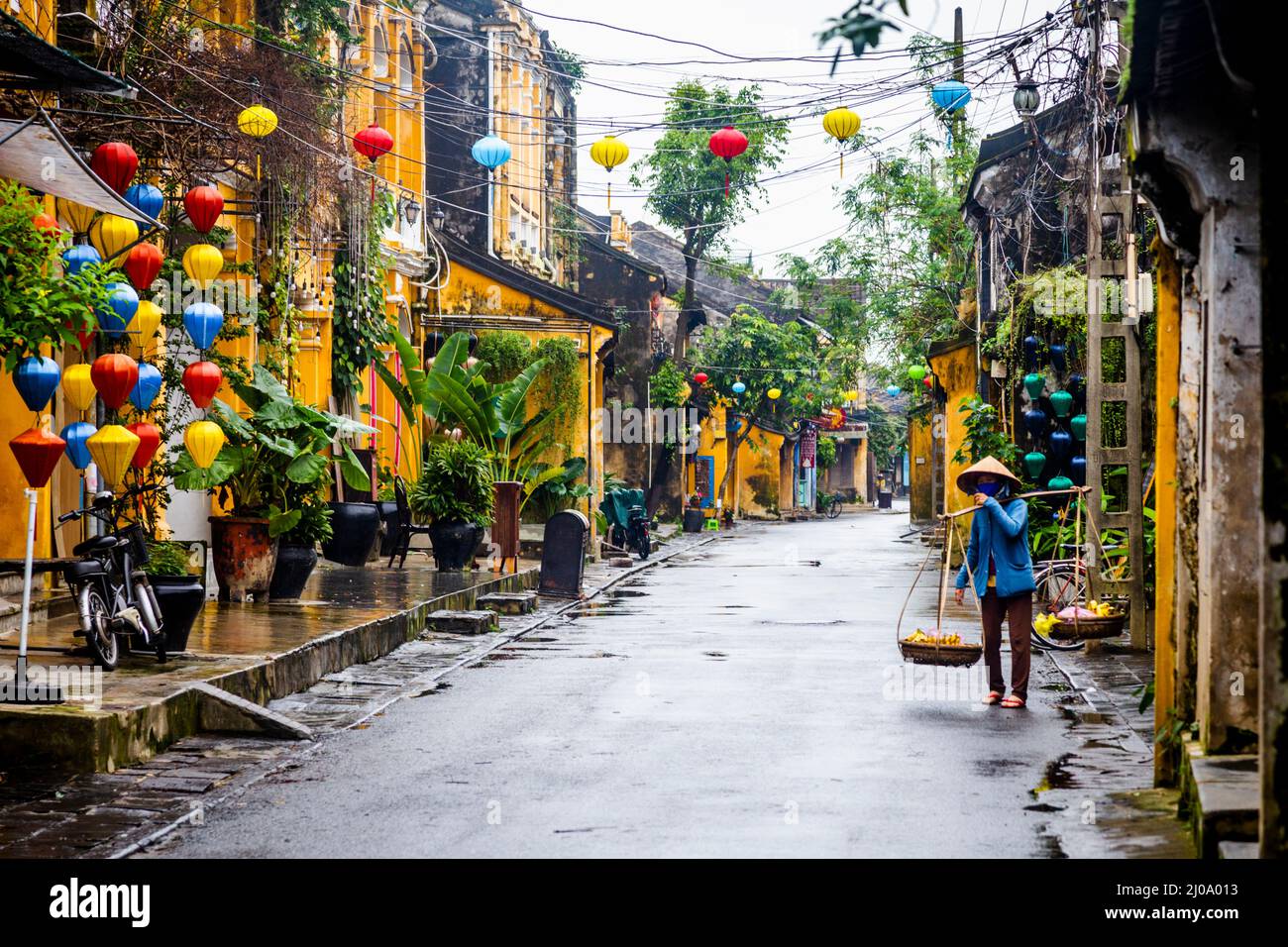 Eine Vietnamesin, die mit ihrem Polenträger eine nasse Straße in der Altstadt entlang geht. Stockfoto