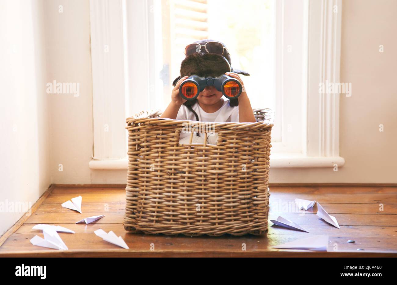 Der Himmel ist klar. Aufnahme eines entzückenden kleinen Jungen, der in einem Korb zwischen Papierdüsen sitzt. Stockfoto