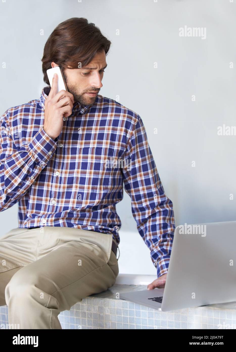 Nachholbedarf bei der Arbeit von zu Hause aus. Ein junger Mann, der am Laptop arbeitet, während er am Telefon telefoniert. Stockfoto