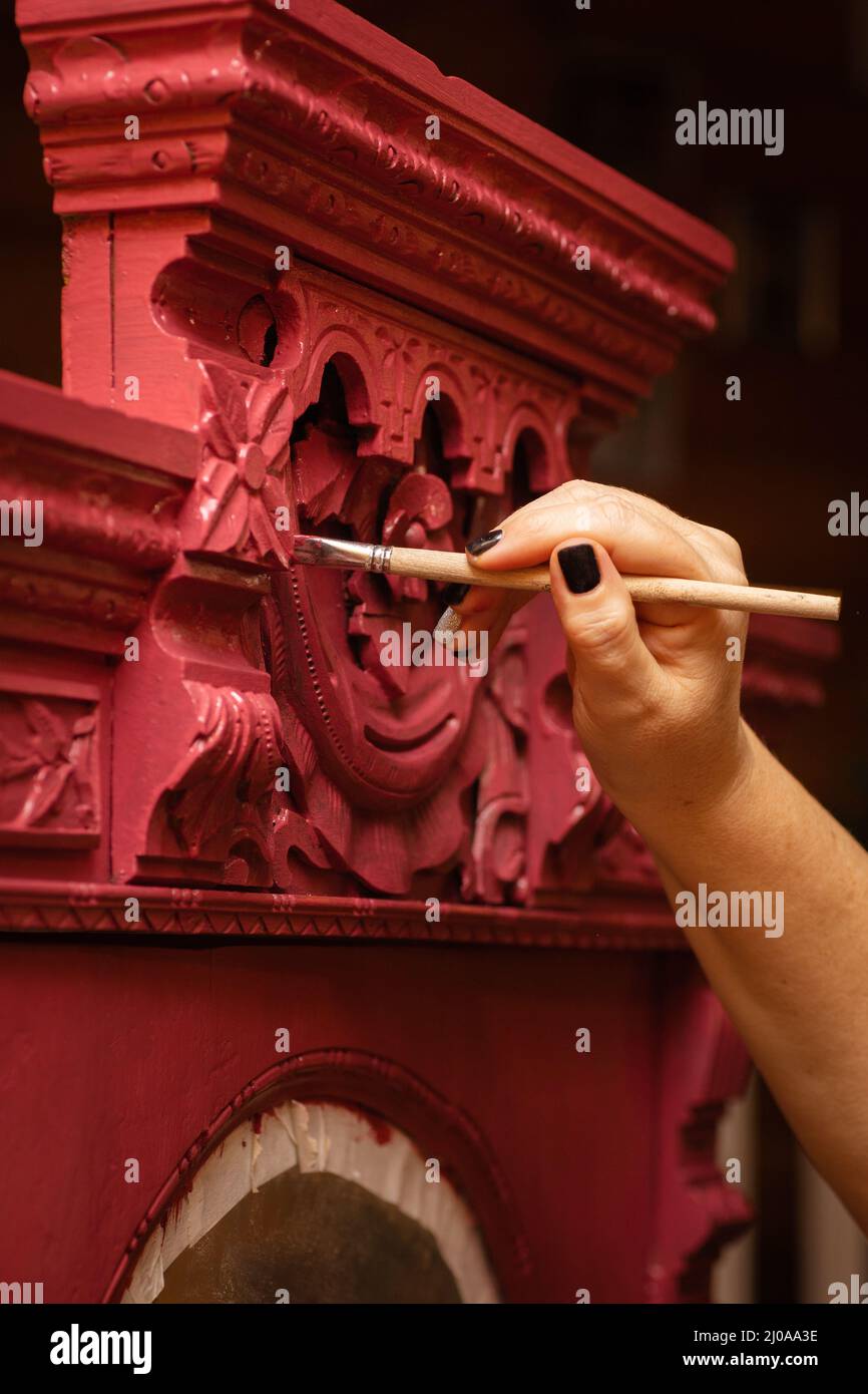 Handbemalung Holzschrank mit schillernden handgefertigten geschnitzten Ornamenten in roter Farbe mit Pinsel in der Werkstatt für die Renovierung von alten antiken Stockfoto