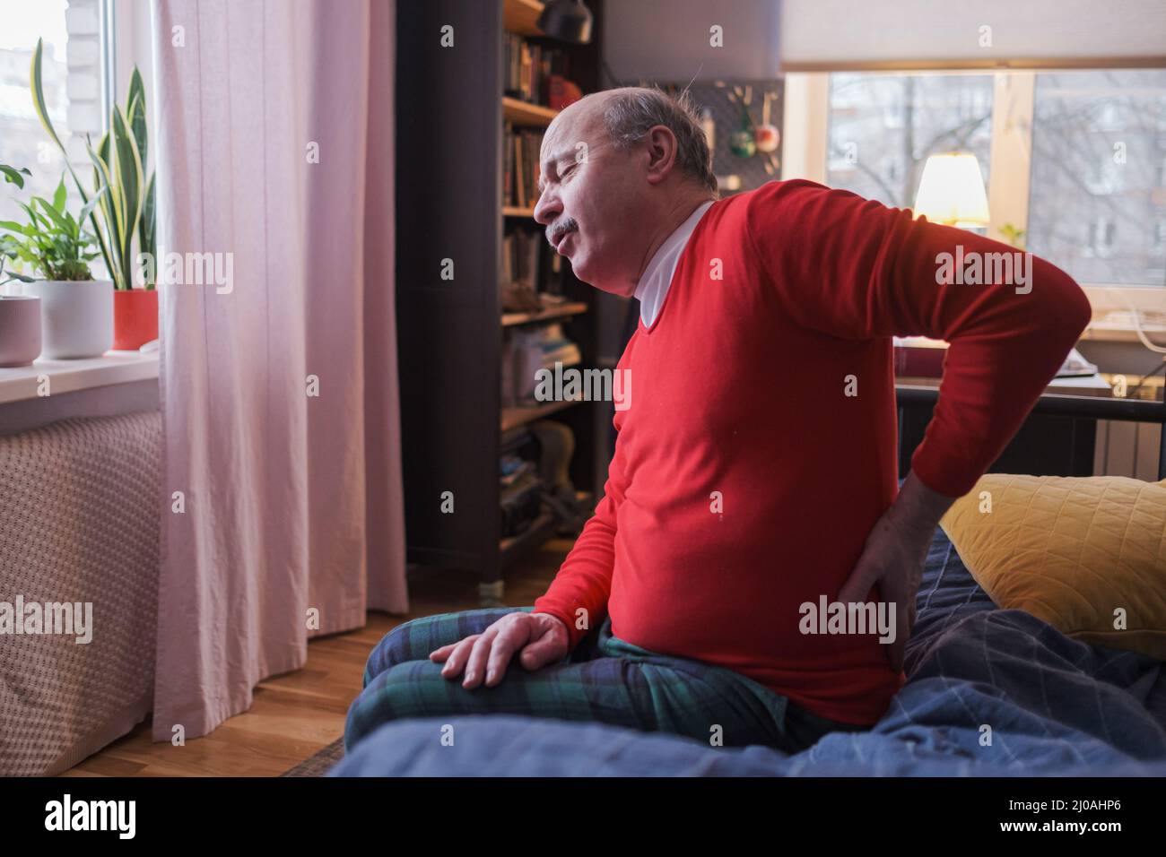 Älterer Mann, der Rückenschmerzen oder Zügel zu Hause auf dem Bett sitzend hatte. Stockfoto
