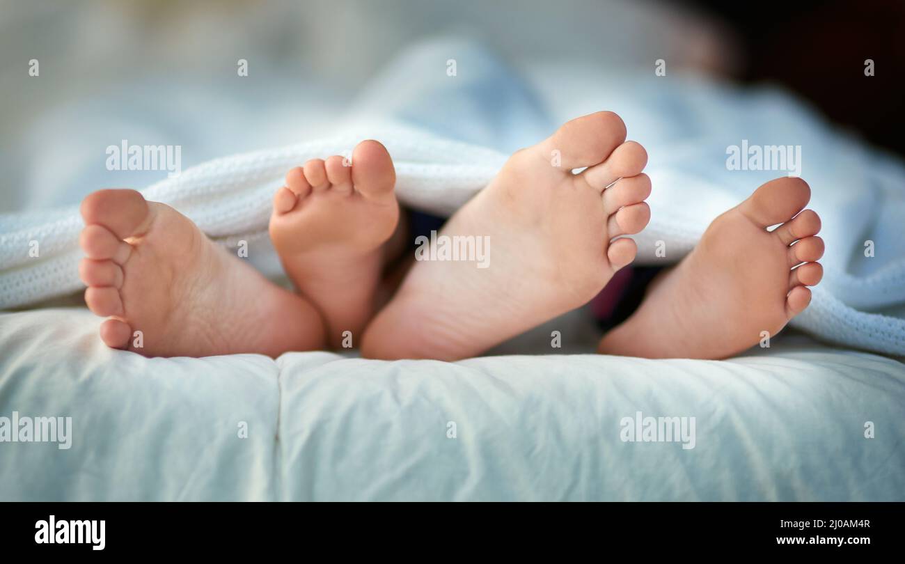 Früh ins Bett, früh zum Aufstehen. Zugeschnittenes Bild von den Füßen eines Elternteils und eines Kindes, die unter den Abdeckungen herausragen. Stockfoto