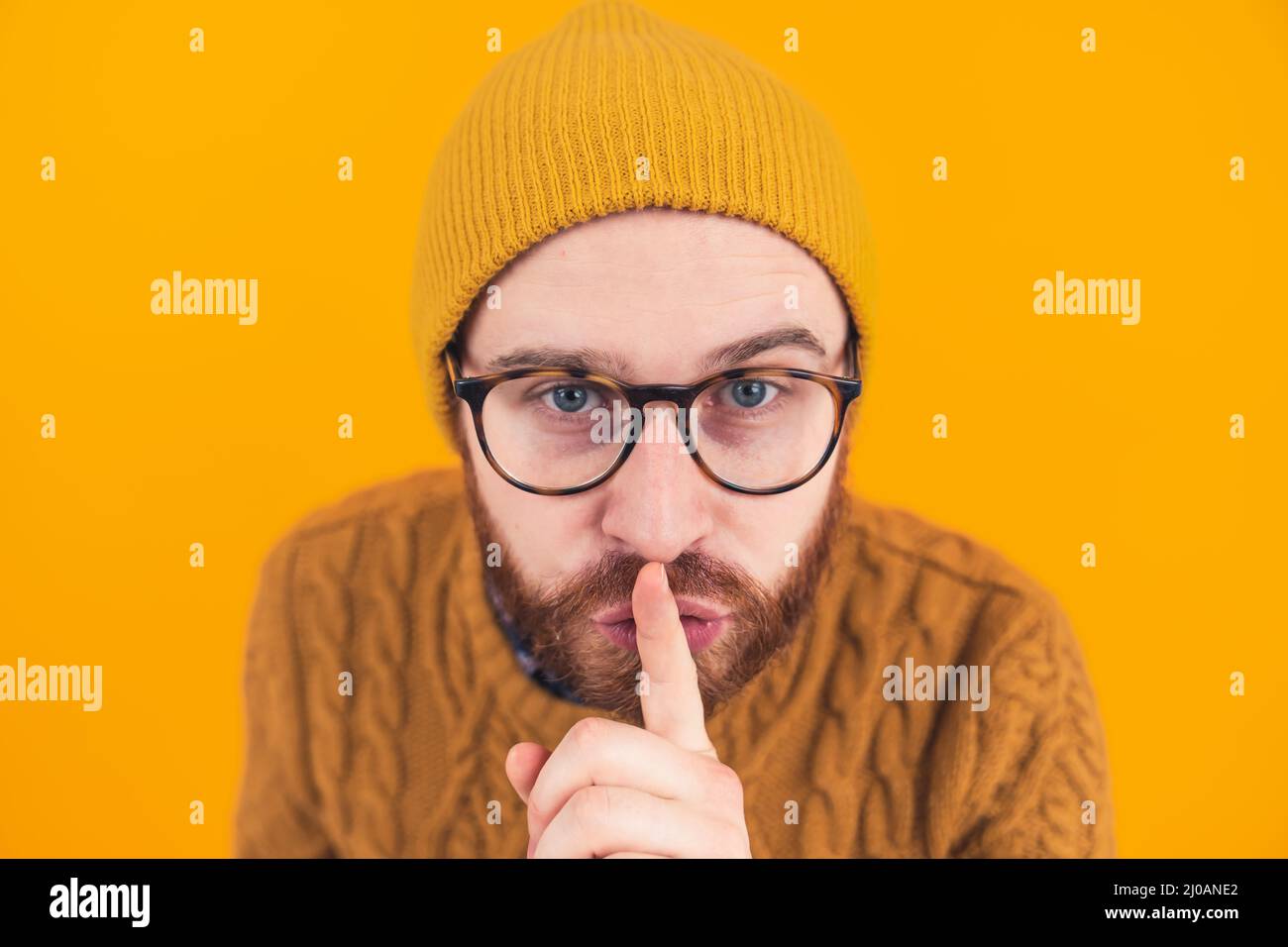 Nahaufnahme eines jungen bärtigen kaukasischen Mannes, der auf die Kamera schaut, die eine Geste mit einem vereinzelten orangenen Hintergrund auf den Kopf zeigt. Hochwertige Fotos Stockfoto