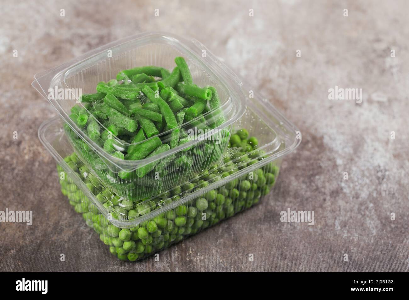 Kunststoffbehälter mit verschiedenen Bio tiefgefrorenen Gemüse auf dem Tisch. Grüne Erbsen und grüne Bohnen in einer Schachtel schneiden Stockfoto