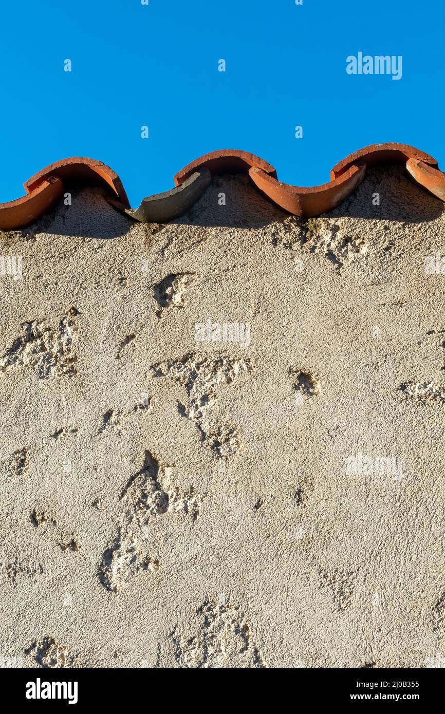 Nahaufnahme einer verwitterten Wand mit einem gekachelten Dach gegen einen klaren blauen Himmel Stockfoto