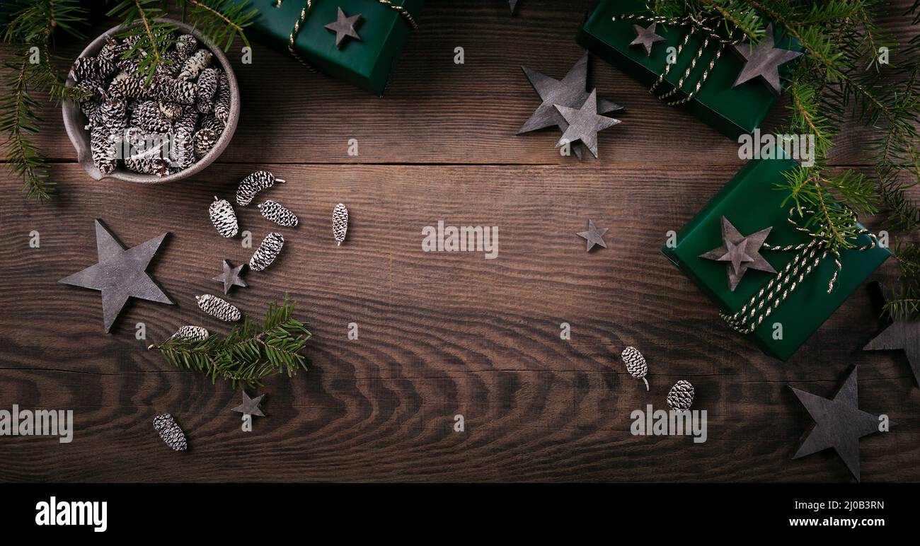 Weihnachtsrahmen mit Geschenkschachteln, Sterndekorationen aus Holz, Tannenzapfen und Fichtenzweigen auf dunklem Holzhintergrund. Urlaub Hintergrund in der natürlichen Erde Stockfoto