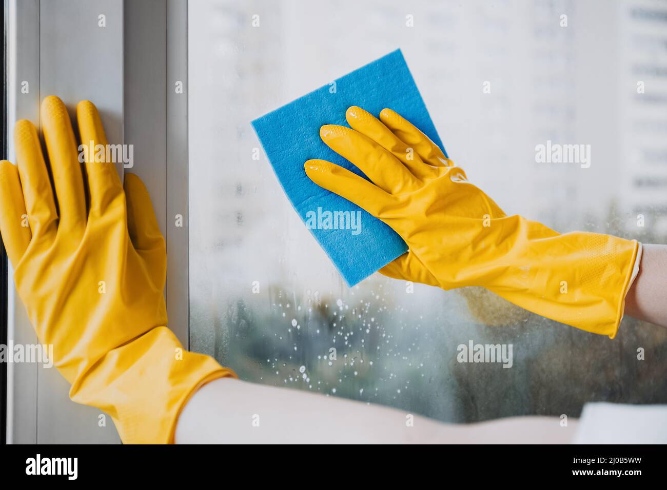Mann in gelben Gummihandschuhen, der das Fenster mit saubereren