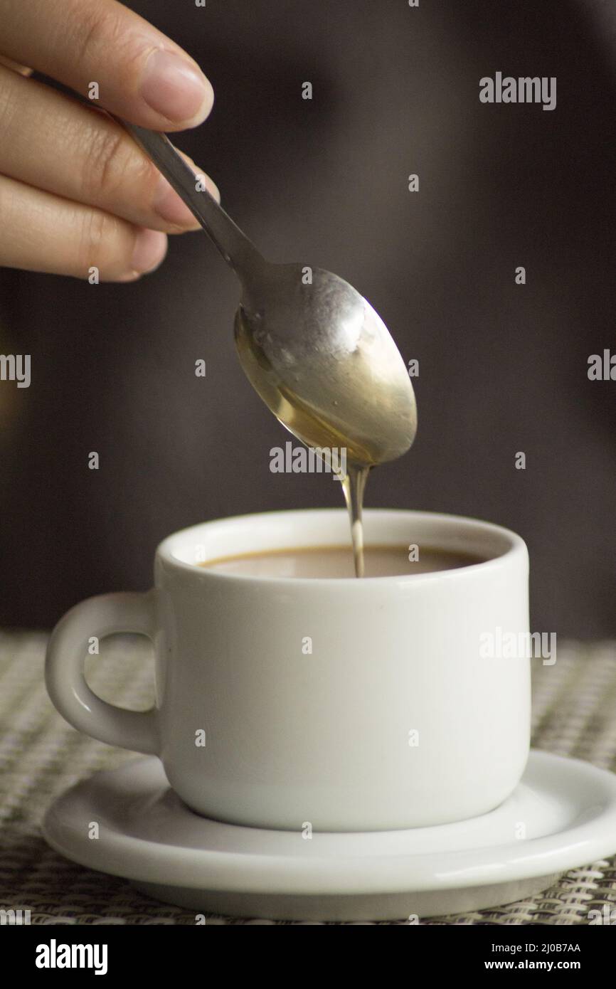 Hand und Löffel Maissirup in einer Tasse Kaffee Espresso Stockfoto