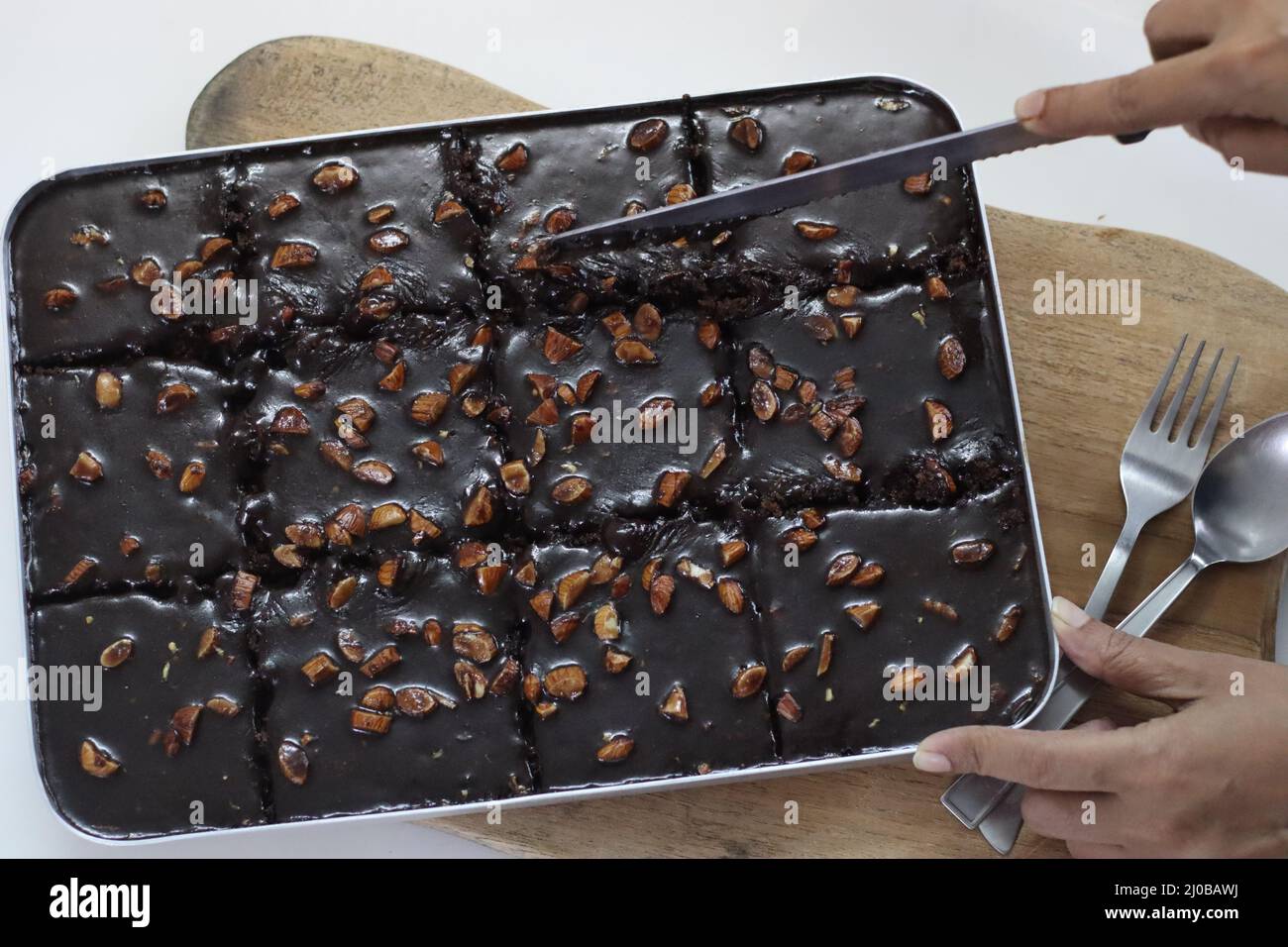 Schneiden von Texas Torte. Butterhaltiger und schokoladiger Kuchen in rechteckige Stücke im Backblech geschnitten. Frisch aus dem Ofen. Aufgenommen auf weißem Hintergrund Stockfoto