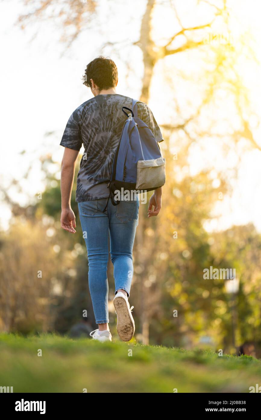 Junger Mann mit einer Tasche, der im Park mit einigen Bäumen im Hintergrund herumläuft Stockfoto