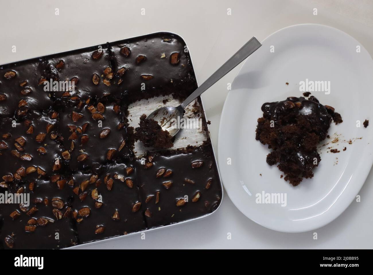Ein Stück Texas-Torte auf einem Teller serviert. Butterhaltiger und schokoladiger Kuchen in rechteckige Stücke im Backblech geschnitten und daraus geschöpft. Aufnahme o Stockfoto
