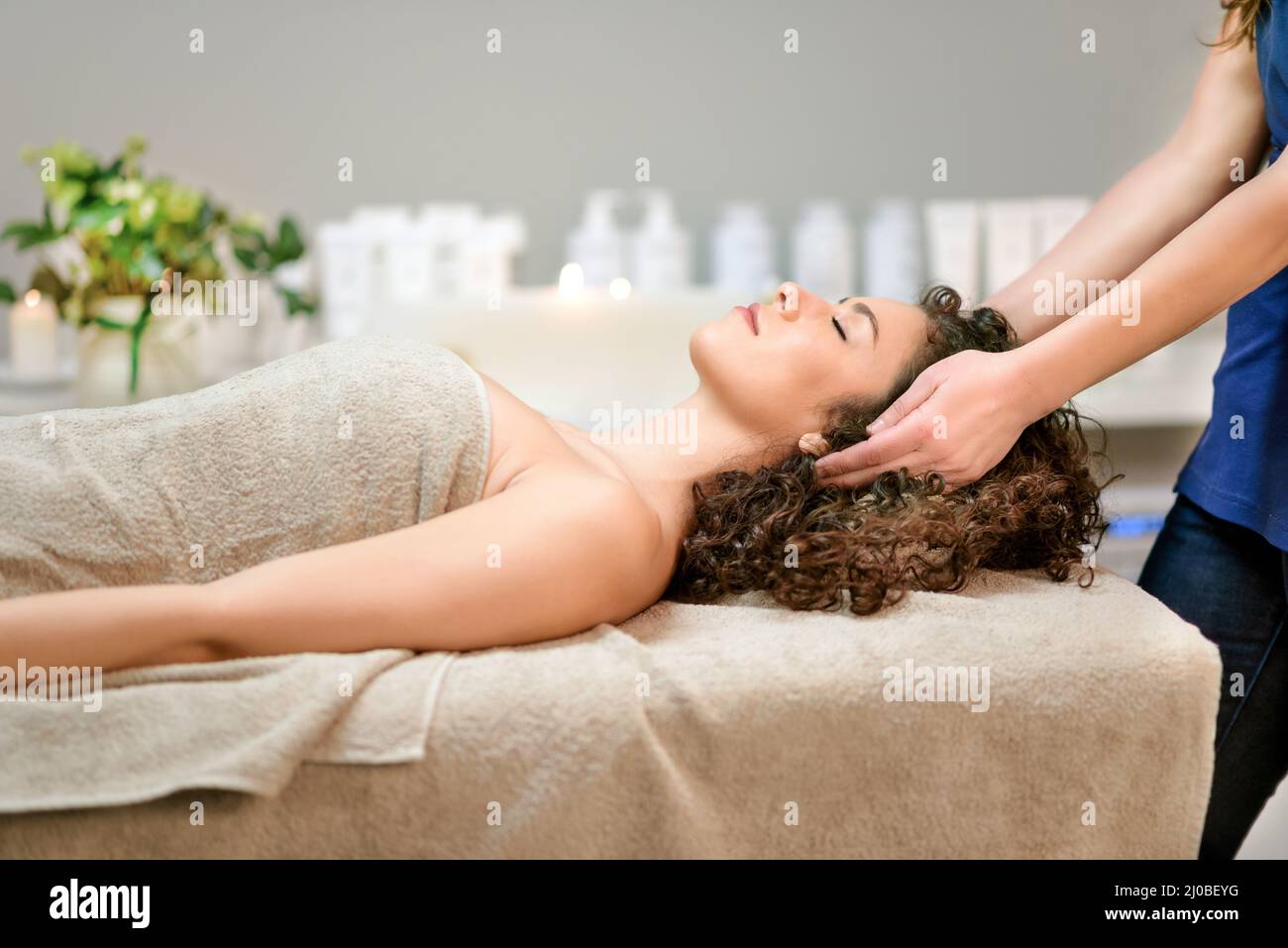 Seitenansicht einer ruhigen Klientin mit geschlossenen Augen, eingewickelt in ein Handtuch, das auf der Couch liegt und während des entspannenden Eingriffs eine Massage im Schönheitssalon genießt Stockfoto