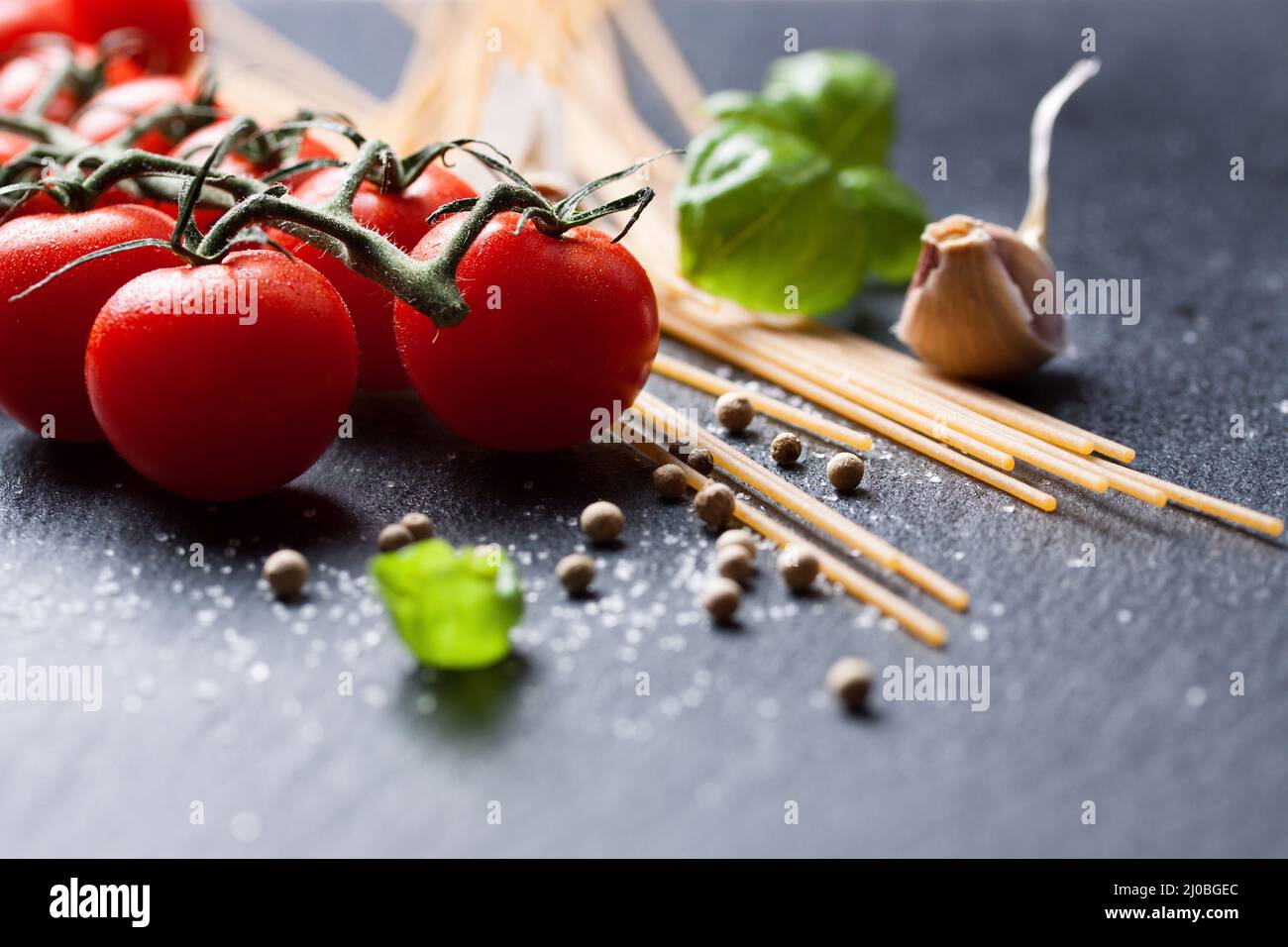 Pasta-Zutaten. Kirschtomaten, Spaghetti, frisches Basilikum, Gewürze auf dunklem Steingrund, Stockfoto