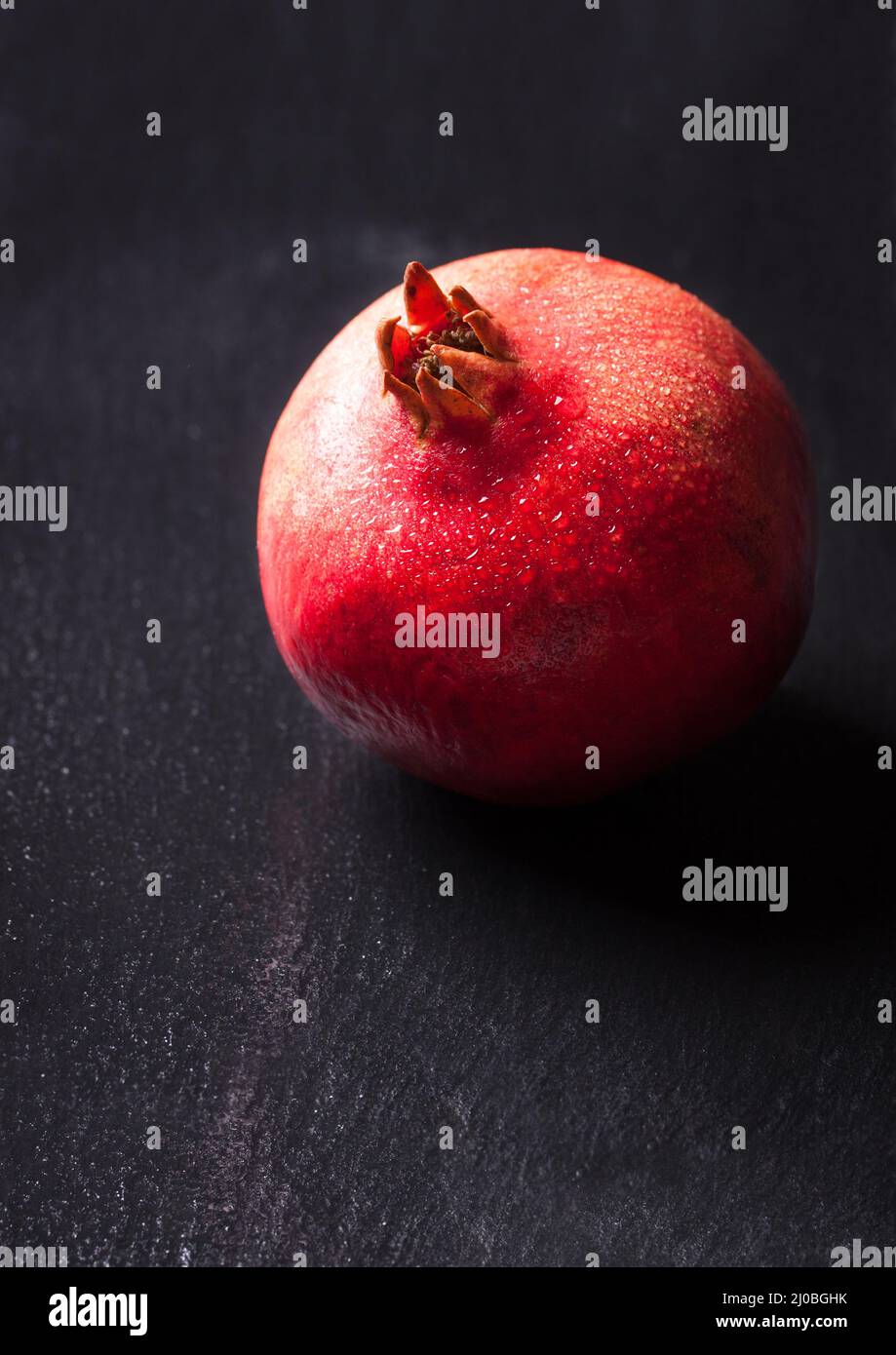 Ganzer, frischer, saftiger Granatapfel mit Wassertropfen auf dunklem Grund Stockfoto