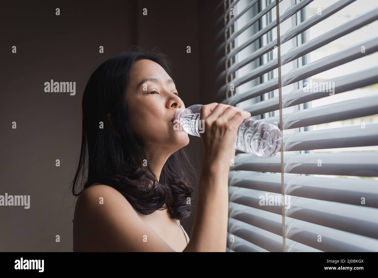Frau trinkt Mineralwasser aus der Flasche nach dem Aufwachen im Schlafzimmer. Stockfoto