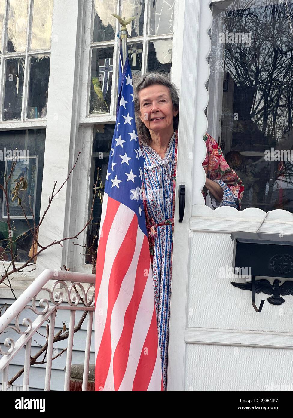 Patriotische 80-jährige Frau mit der amerikanischen Flagge am Vordereingang in Brooklyn, New York. Stockfoto